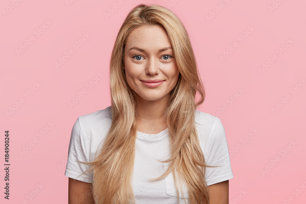 Photo of confident pleasant looking pleased female with blonde long hair poses in pink studio, wears casual clothes, being happy to recieve praising words from boss for good work and diligence Photo of confident pleasant looking pleased female with blonde long hair poses in pink studio, wears casual clothes, being happy to recieve praising words from boss for good work and diligence