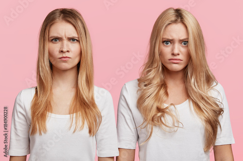 Grumpy dissatisfied female students have displeased expressions after failing exams or session at unversity  look with displeasure  isolatd over pink background. Discontent annoyed beautiful women
