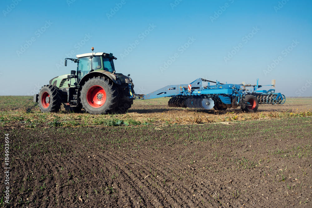 Fototapeta premium Modern tractor in a field on a sunny day. Tractor preparing land for sowing
