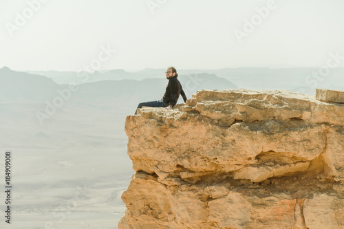 Alone man sitting at the edge of cliff in the desert