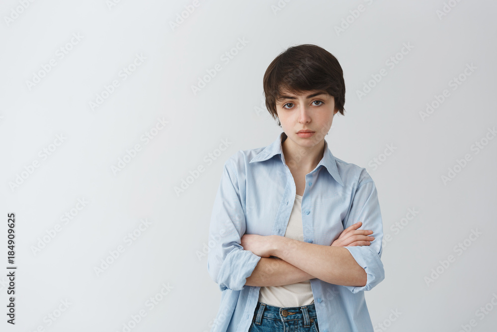 Portrait of good-looking masculine girl with short dark hair and brown big eyes, crossing hands, having aggressive and confident look. Portrait of good-looking masculine girl with short dark hair and brown big eyes, crossing hands, having aggressive and confident look.