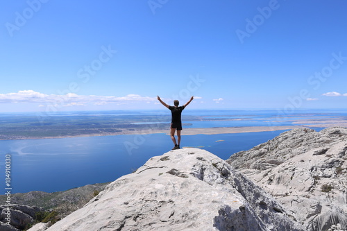 Silhouette of happy man standing on rock and arms outstretched against the sky