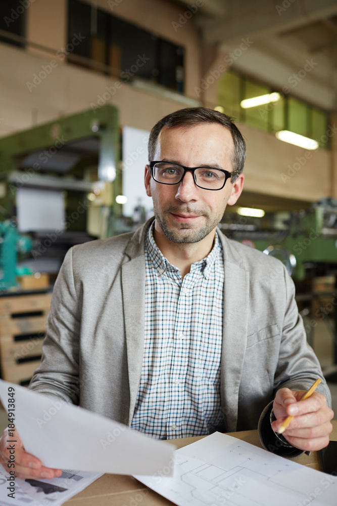 Successful engineer in formalwear and eyeglasses looking at camera while working with papers
