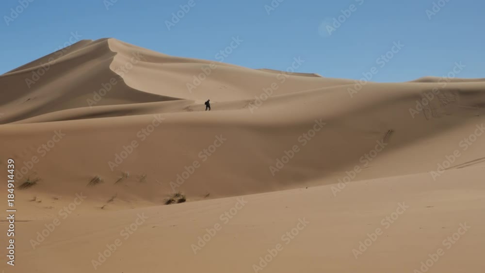 Man walking in desert dunes with sunset landscape in Moroccon desert Man walking in desert dunes with sunset landscape in Moroccon desert