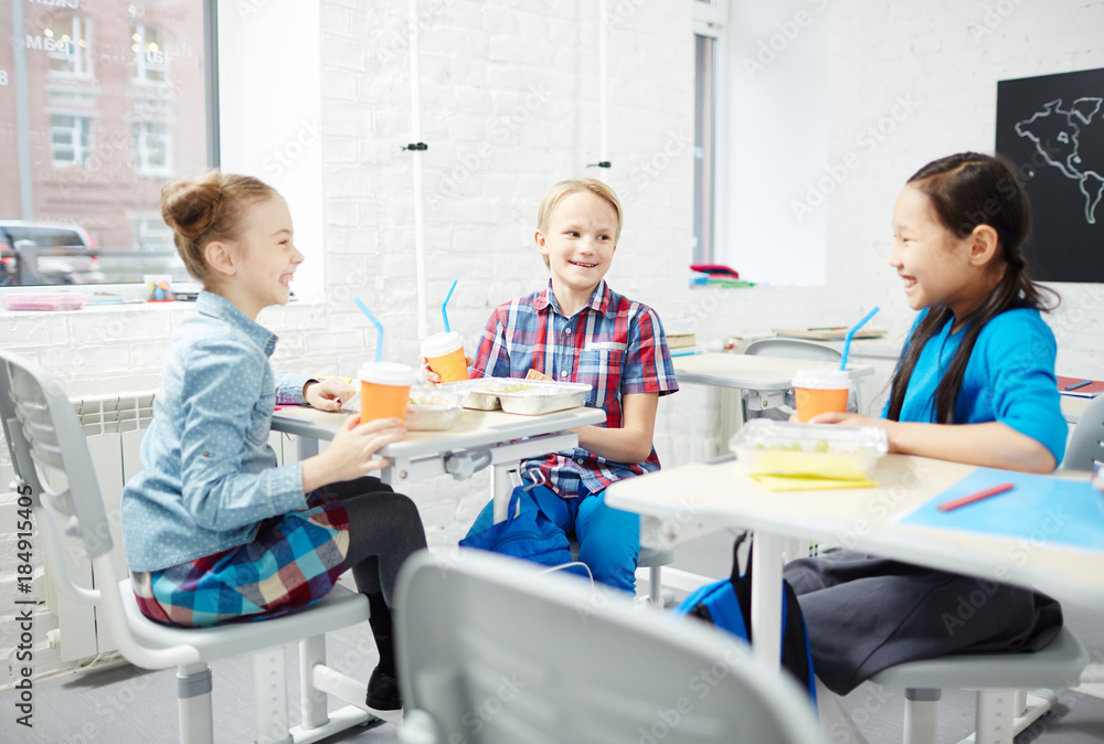 Three friendly schoolmates having talk during lunch in classroom at break Three friendly schoolmates having talk during lunch in classroom at break