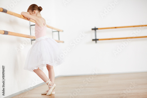 Little ballerina keeping her head on bar while feeling upset during training