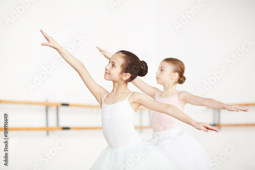 Two little girls stretching their arms during ballet exercise in classroom