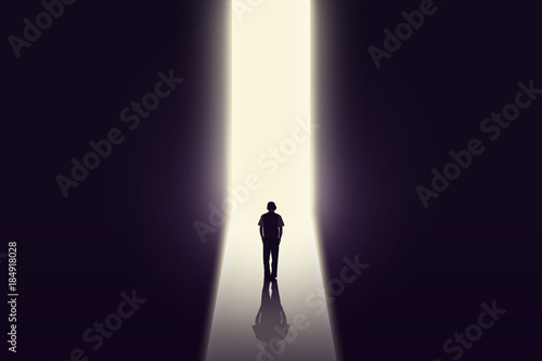 Young businessman stands in dark tunnel and looks in the glowing end