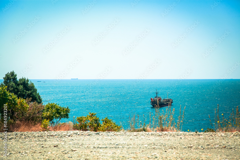 Some kind of merchant ship is at anchor near the shore of the Black sea. The ship is well visible from the height of the picturesque cliff