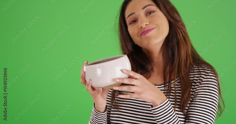 Portrait of cheerful Latina female holding up ceramic bowl, smiling at camera on green screen. On green screen to be keyed or composited. Portrait of cheerful Latina female holding up ceramic bowl, smiling at camera on green screen. On green screen to be keyed or composited.