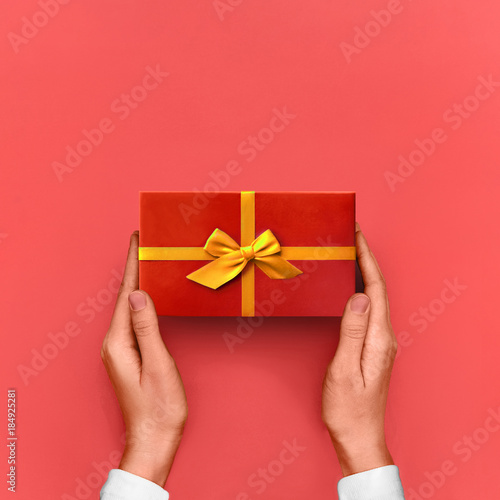 Gift box Bright styled photo Female hands are holding a red gift box with yellow ribbon in gesture of giving on pink background Top view Photo mockup with space for text © Picture Store