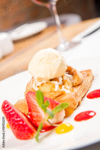Apple pie with ice-cream decorated with a strawberry, fruit sauce and herb served in a restaurant
