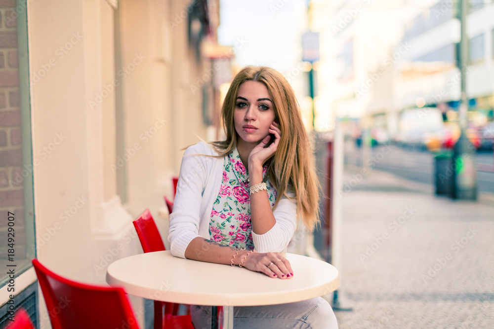 Blond girl sits at the empty table of a street cafe