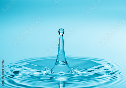 Splash and crown on rippled blue liquid or water surface . Water splash with a crown and reflection
