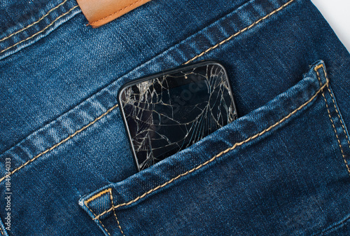 Mobile phone with a broken screen in the pocket of blue jeans.