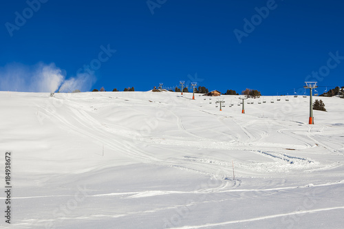 Chairlift without people. Artificial snowing ski slope by Snow cannon maker.