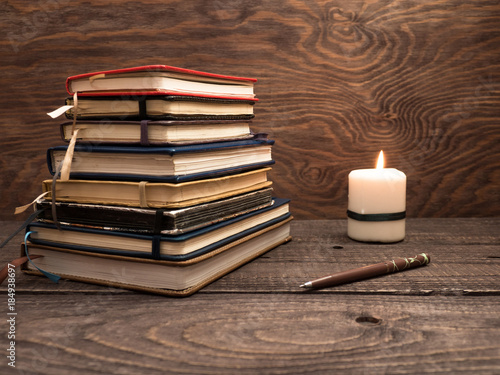 A stack of notebooks, a pen and a candle on a wooden table