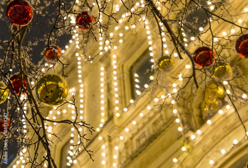 golden red shiny balls on a branch against the backdrop of the house decorated with a glowing garland, an evening walk on the eve of Christmas street decorations