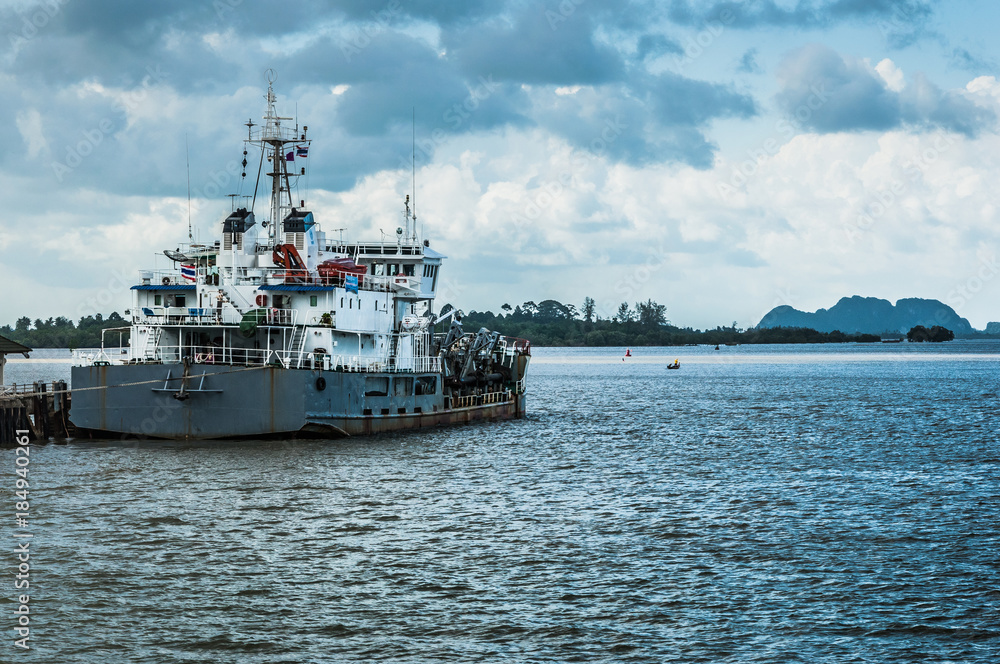 Grey commercial boat near the pier with dramatic sky on the background