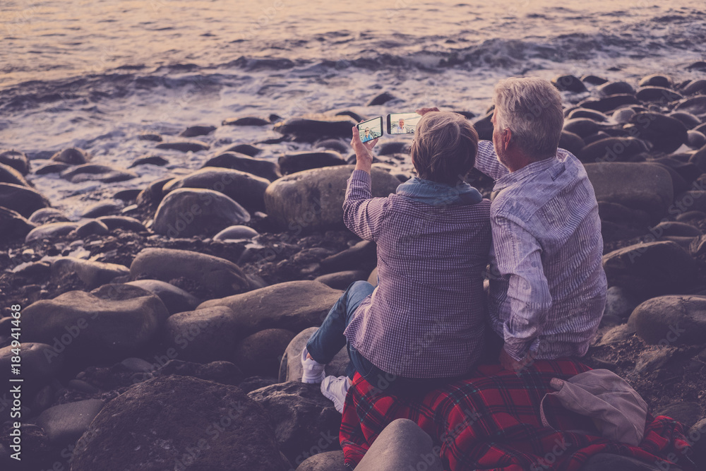 couple of adults sitting at the beach looking at the phone and taking pictures couple of adults sitting at the beach looking at the phone and taking pictures