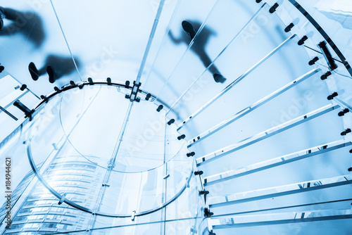 Silhouettes of people walking on a glass spiral staircase