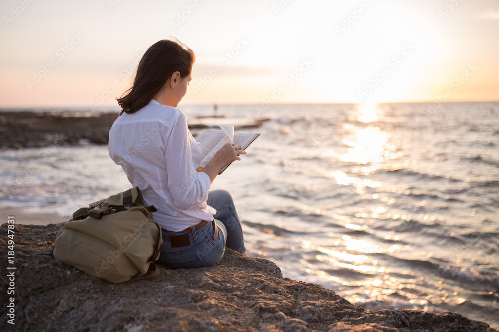 teenage girl reading book on the beach in sunset