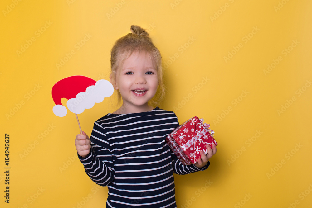 Pretty smiling little girl with santa hat and gift box on yellow background Pretty smiling little girl with santa hat and gift box on yellow background