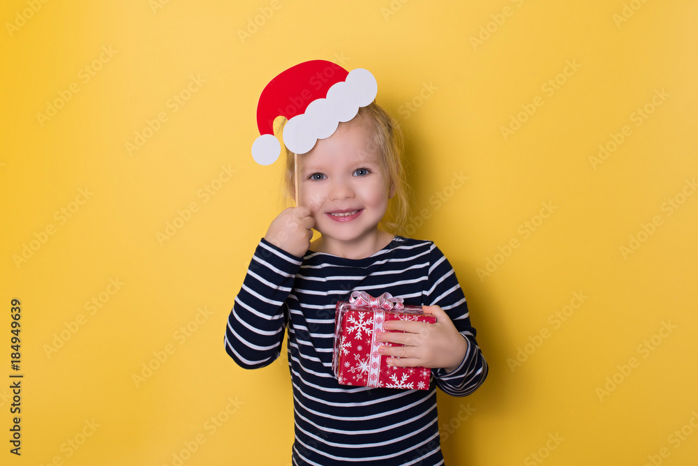 Pretty smiling little girl with santa hat and gift box on yellow background Pretty smiling little girl with santa hat and gift box on yellow background
