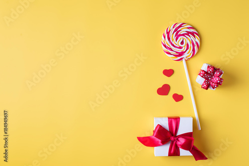 Valentine's day bright yellow background, greeting card concept, lollipop or sweet candy on sticks, with gift box, decorative hearts.