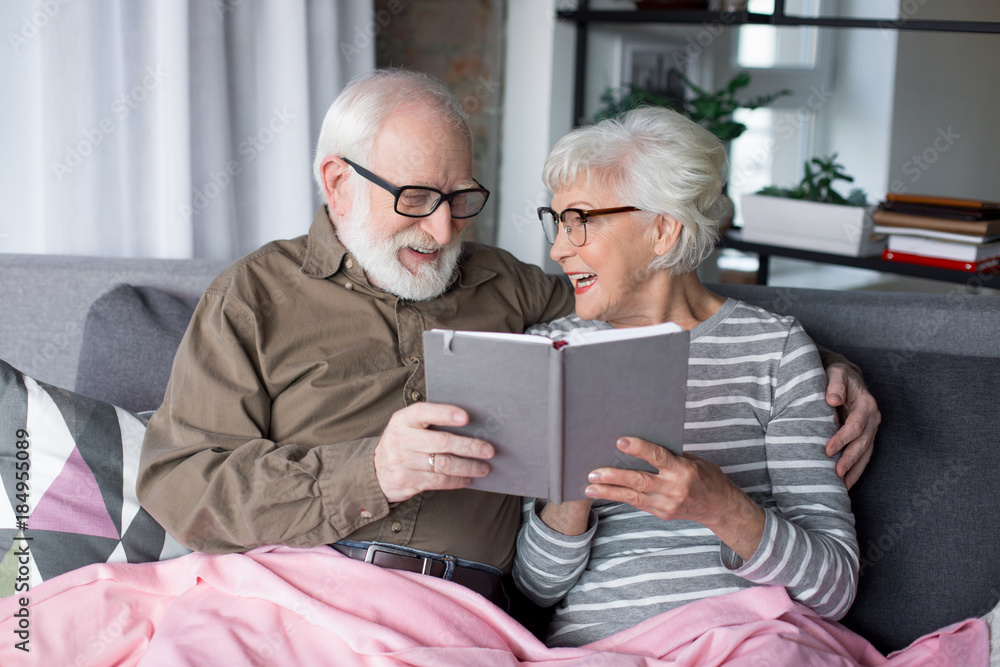 Sweet memories. Waist up portrait of smiling old sweethearts in glasses looking into notebook. They are laughing while wife is showing one funny sketch to beloved husband Sweet memories. Waist up portrait of smiling old sweethearts in glasses looking into notebook. They are laughing while wife is showing one funny sketch to beloved husband