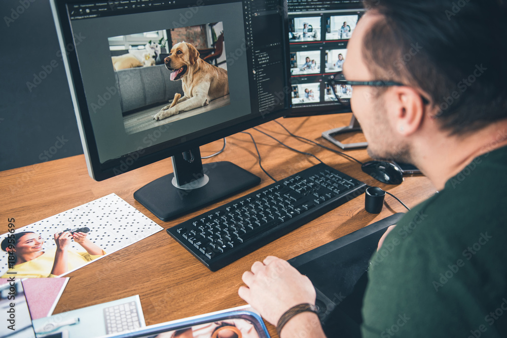 Side view bearded man having job with picture of cute dog in digital device while sitting at table in office. Profession concept - obrazy, fototapety, plakaty 