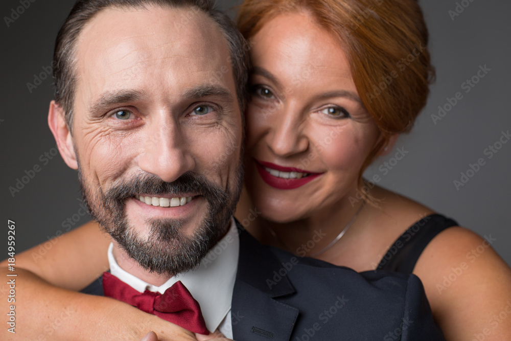 Portrait of happy married couple standing and hugging. They are looking at camera with joy and smiling. Lovers are wearing formal clothing Portrait of happy married couple standing and hugging. They are looking at camera with joy and smiling. Lovers are wearing formal clothing