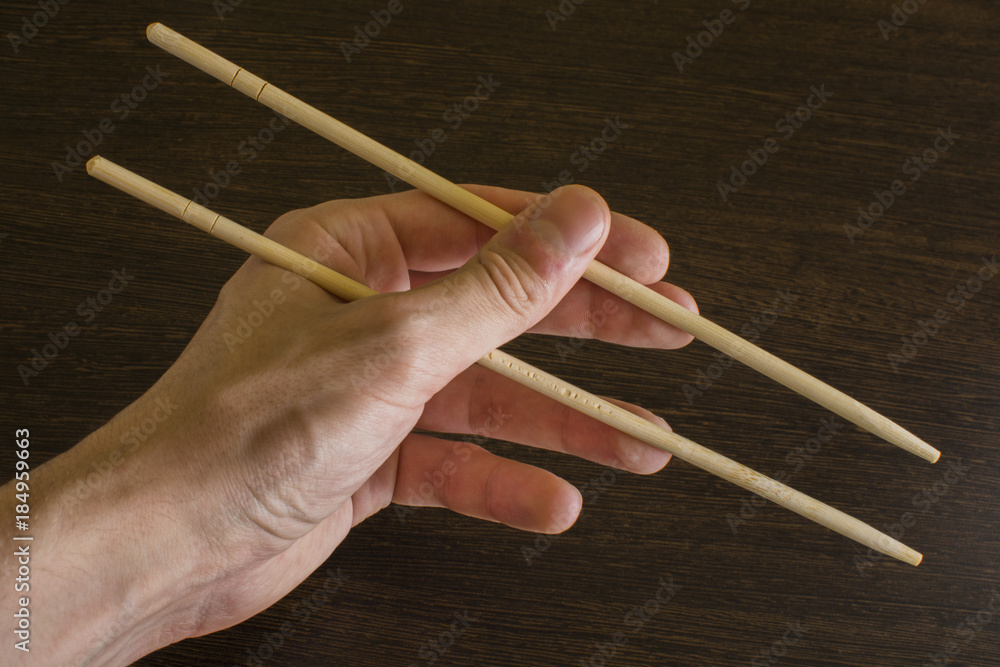 The left hand of a man using bamboo chopsticks on a wooden background The left hand of a man using bamboo chopsticks on a wooden background
