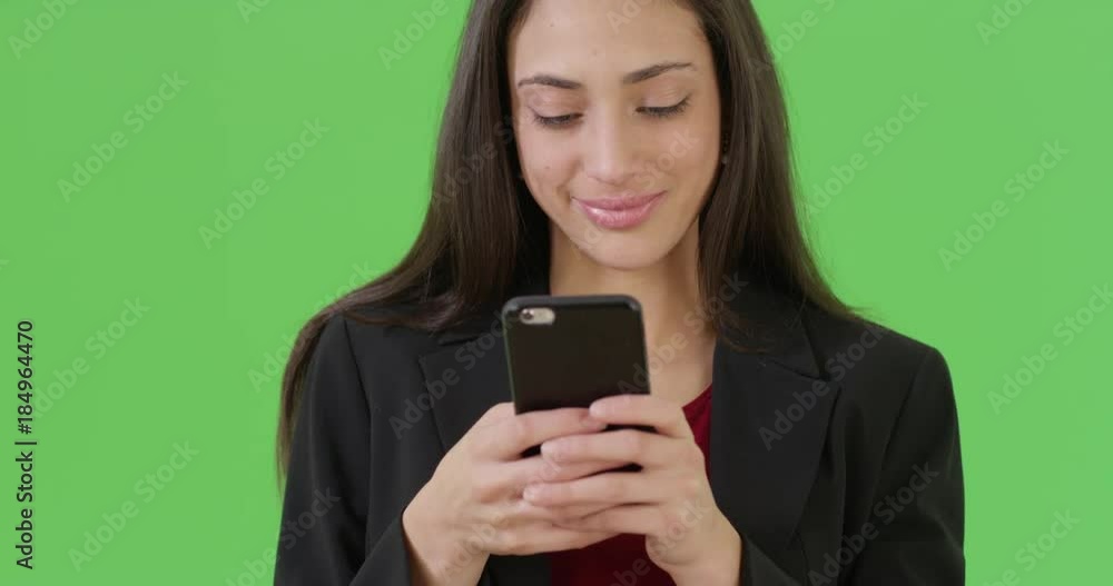 A Latina office professional texts on her mobile phone on green screen. On green screen to be keyed or composited. A Latina office professional texts on her mobile phone on green screen. On green screen to be keyed or composited.
