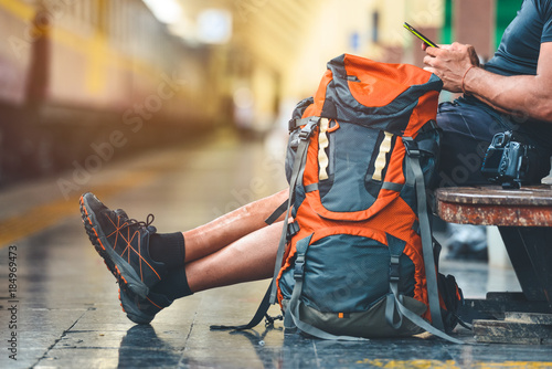 Tourist man with a backpack in the train station holding a smart phone. A camera on the bench. Digital nomad traveler concept