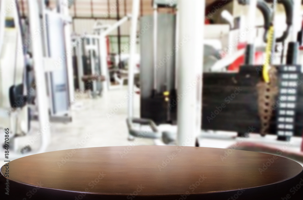 Fototapeta premium Wooden table on blurred background of fitness gym interior of modern club with equipment for your photomontage or product display.