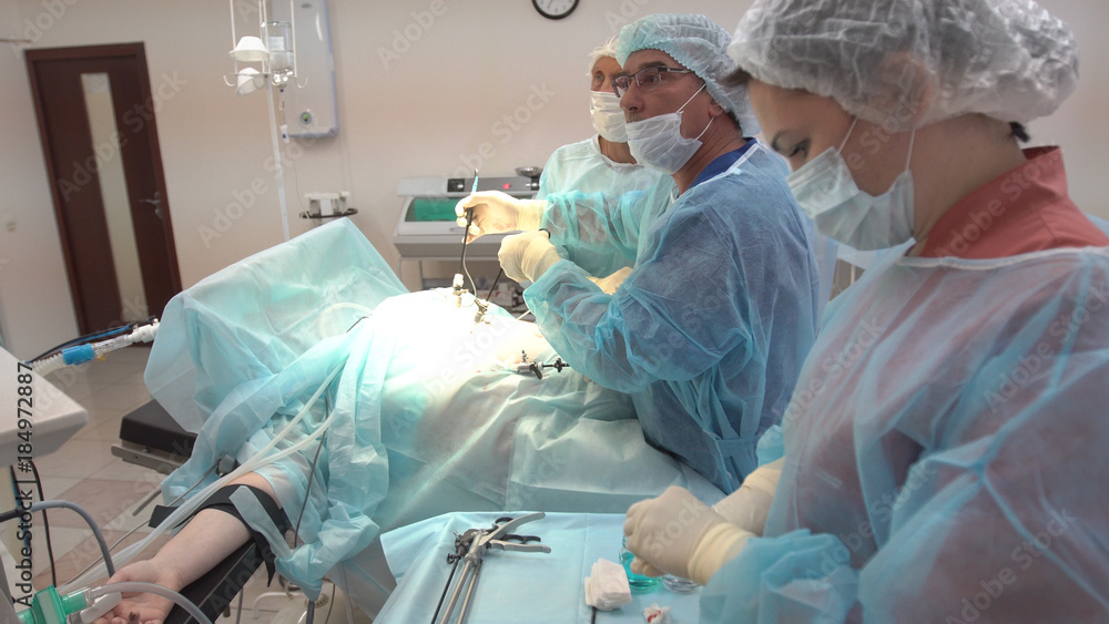 Surgeons team working with Monitoring of patient in surgical operating room. Operation using laparoscopic equipment. Hospital. Surgeons team working with Monitoring of patient in surgical operating room. Operation using laparoscopic equipment. Hospital.