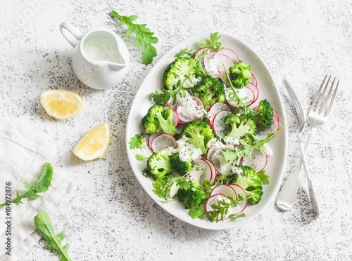 Broccoli and radish salad with yogurt sauce on a light background, top view. Delicious healthy vegetarian food concept