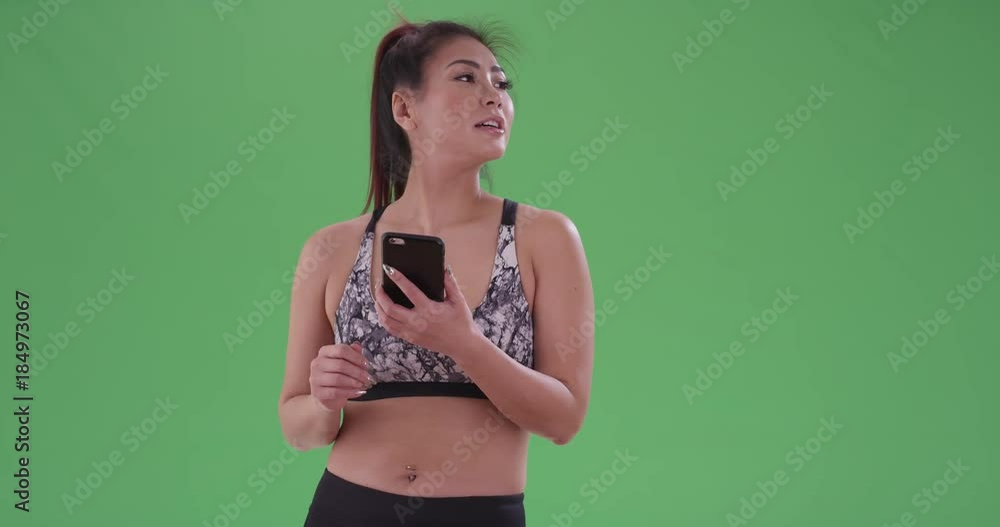 An Asian woman looking around on her phone on green screen. On green screen to be keyed or composited. An Asian woman looking around on her phone on green screen. On green screen to be keyed or composited.