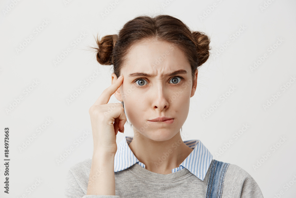 Studio shot of thoughtful caucasian woman in casual holding finger at her temple posing with meaningful look. Young female having confused pensive emotions pondering about her lifestyle Studio shot of thoughtful caucasian woman in casual holding finger at her temple posing with meaningful look. Young female having confused pensive emotions pondering about her lifestyle
