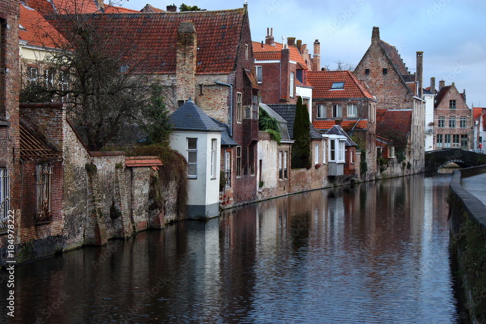 Old town Brugge (Bruges), Belgium. Medieval buildings exterior with tiled roofs and reflection in river canal. Brick ancient houses and walls. Medieval architecture in Europe while travel.  