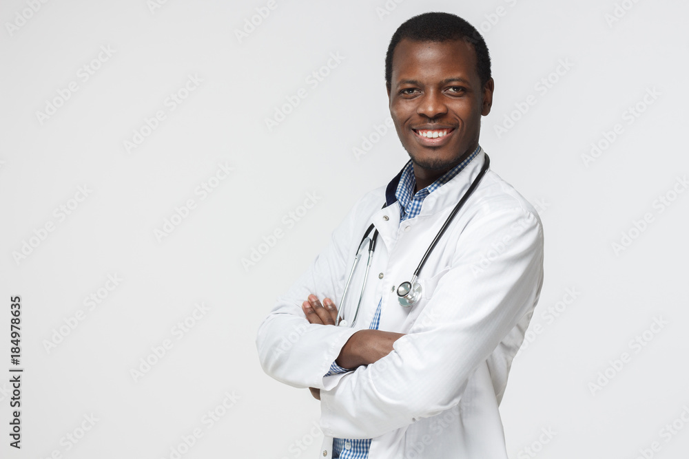 Smiling african american doctor posing with arms crossed, wearing a stethoscope, isolated on grey background Smiling african american doctor posing with arms crossed, wearing a stethoscope, isolated on grey background