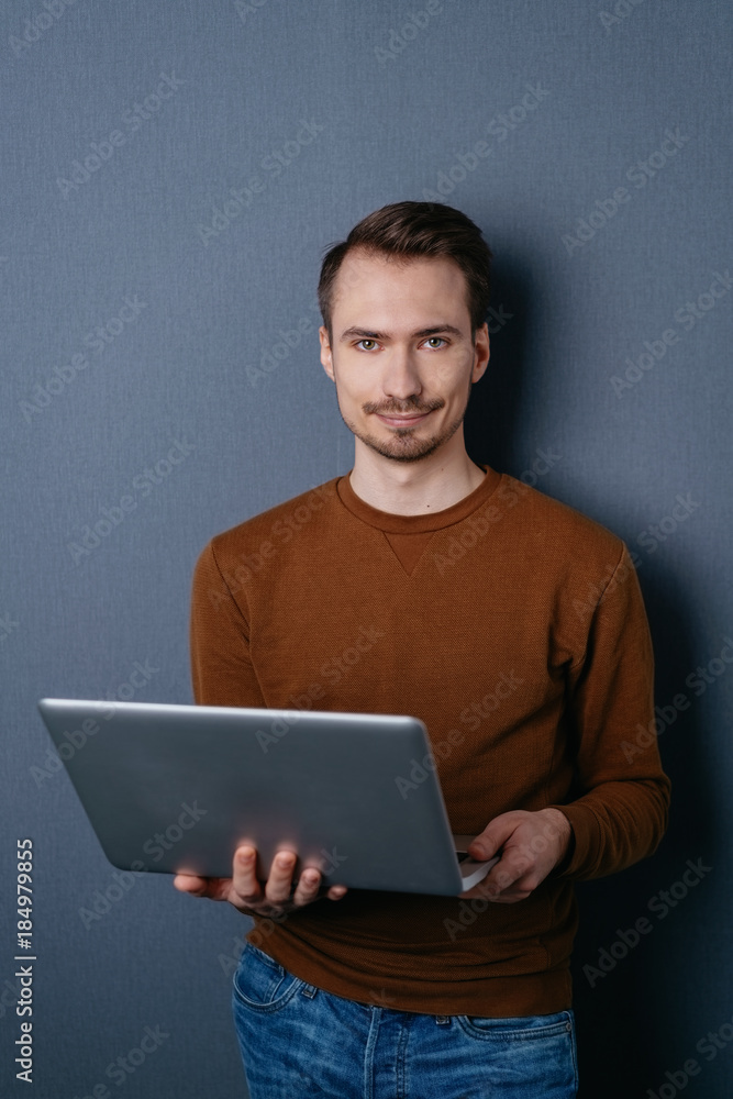 Young man standing with laptop on dark background Young man standing with laptop on dark background