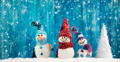 little knitted snowmans on soft snow on blue background