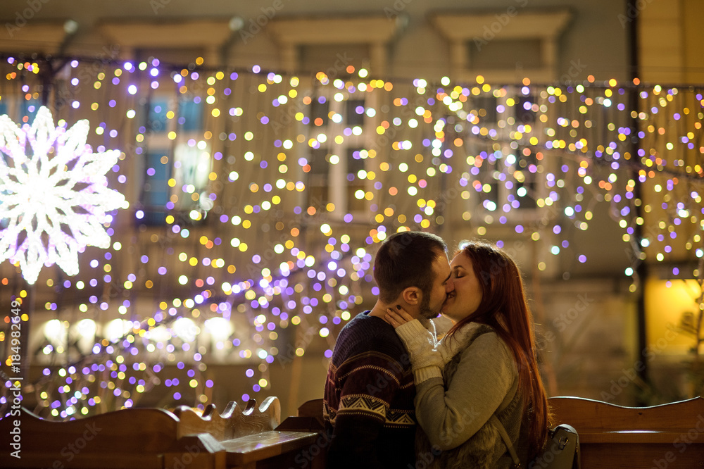 Lovers kiss on the background of shining festive garlands.