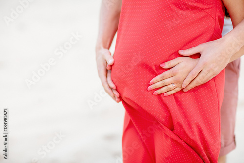 Cropped image of beautiful pregnant woman and her handsome husband hugging the tummy.