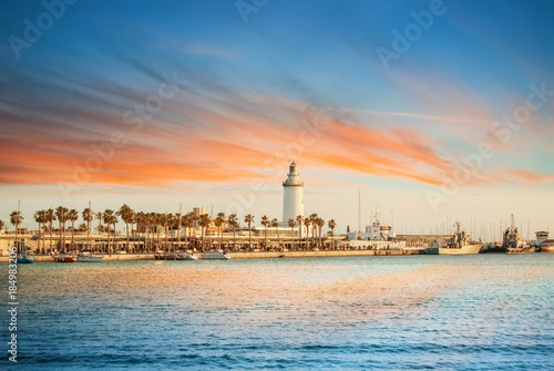 Evening panoramic aerial top view to a promenade with palms, shops and yachts and a lighthouse by the sea with dramatic colorful evening sunset sky at the background. Holiday vacation by the sea.