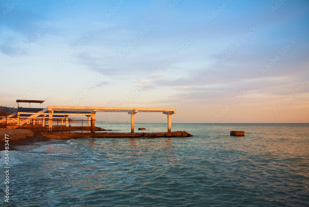 Old vintage  rusty abandoned broken city pier at the sandy bay beach near beautiful sea ocean transparent water in the evening sunlight