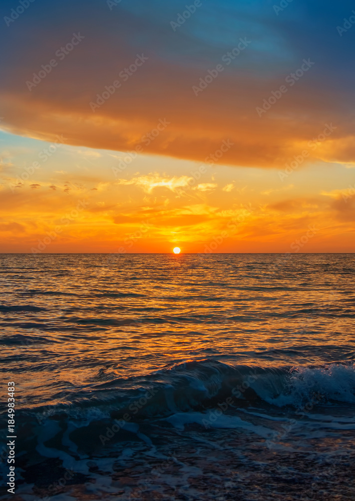 Fototapeta premium A beautiful bright colorful seascape with setting sun, colorful evening twilight landscape, abstract background of holiday relaxing vacation by the sea. Waves at the foreground.