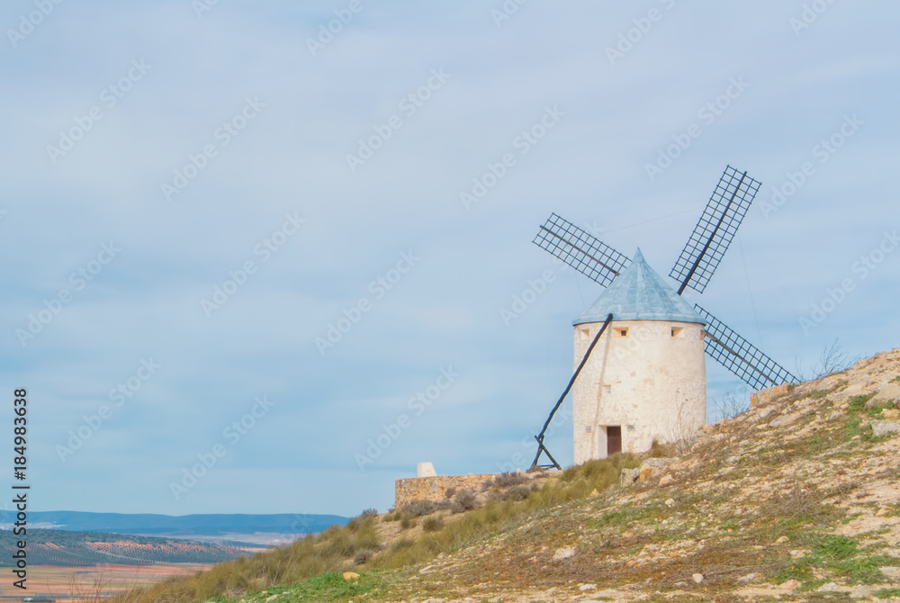 Old white traditional windmill on the hill near Consuegra (Castilla La Mancha, Spain), a symbol of region and journeys of Don Quixote (Alonso Quijano) on cloudy day.